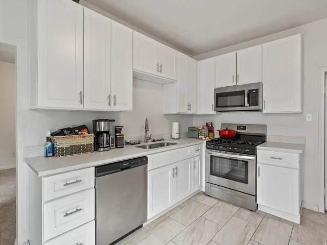 Kitchen with white cabinets, stainless steel appliances, and light stone counters