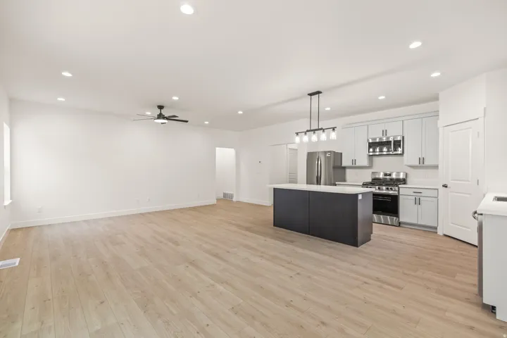 Kitchen with open floor plan, a center island, stainless steel appliances, pendant lighting, and light wood-style flooring