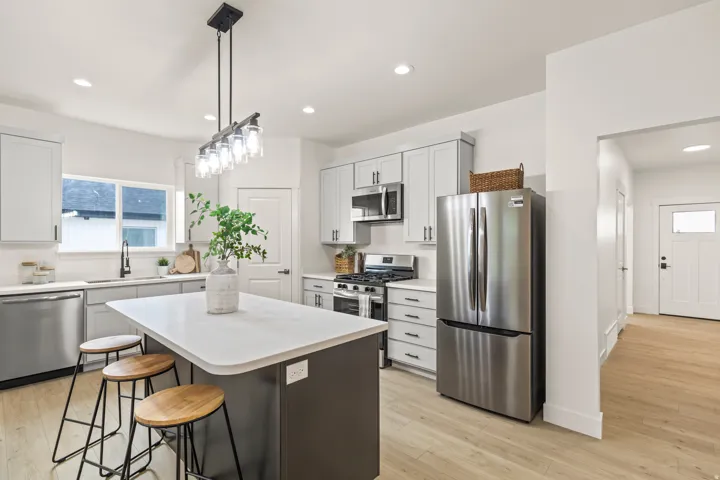 Dual tone kitchen featuring stainless steel appliances, light wood-style floors, a kitchen bar, a kitchen island, and plenty of natural light