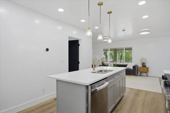 Kitchen featuring a center island with sink, light wood-style flooring, decorative light fixtures, gray cabinetry, and stainless steel appliances