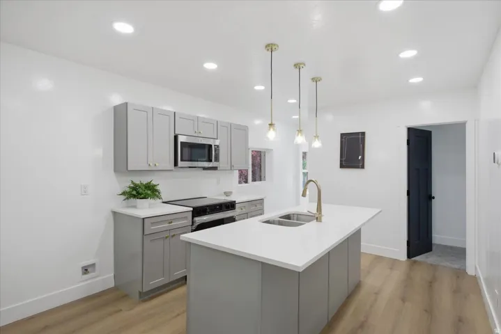 Kitchen featuring gray cabinets, a kitchen island with sink, light wood finished floors, and black range with electric cooktop
