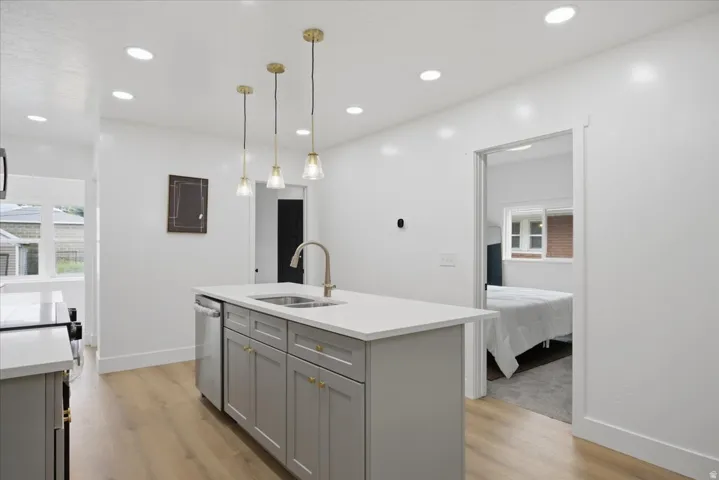 Kitchen with gray cabinets, a center island with sink, decorative light fixtures, light stone counters, and light wood-style flooring