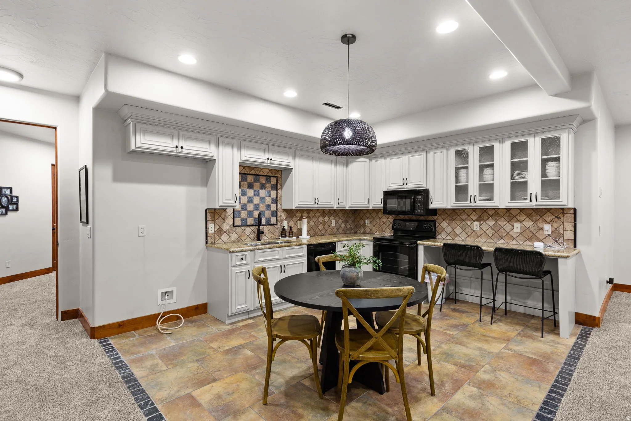 Kitchen featuring glass insert cabinets, white cabinetry, decorative backsplash, black appliances, and stone tile floors