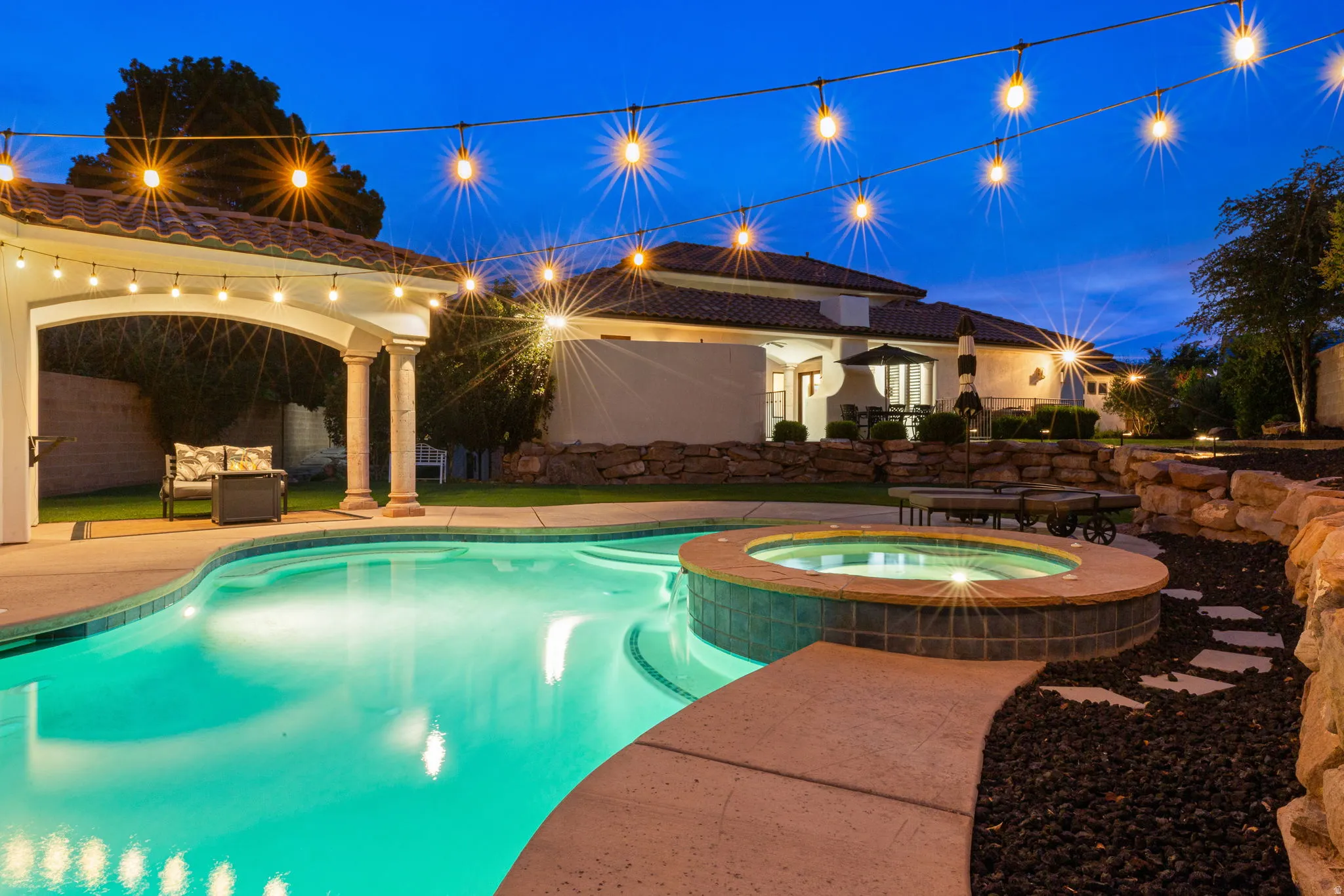 Resort-style backyard featuring a free-form swimming pool, integrated spa, and an arched covered patio with string lighting