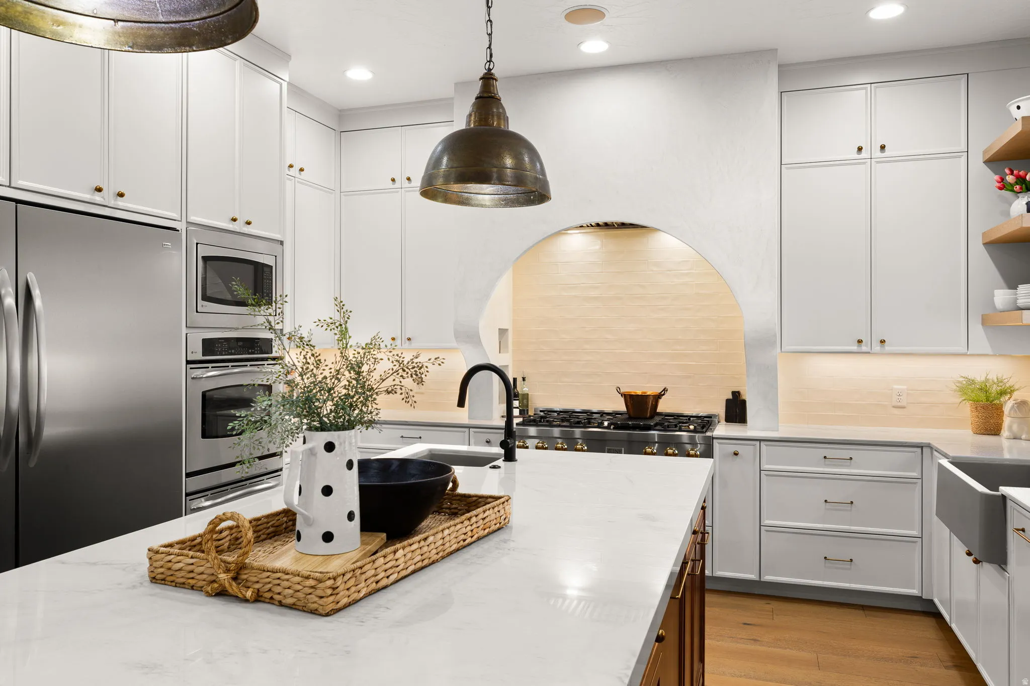 Dual tone kitchen featuring dual tone cabinetry, stainless steel appliances, light wood finished floors, light stone counters, and open shelves
