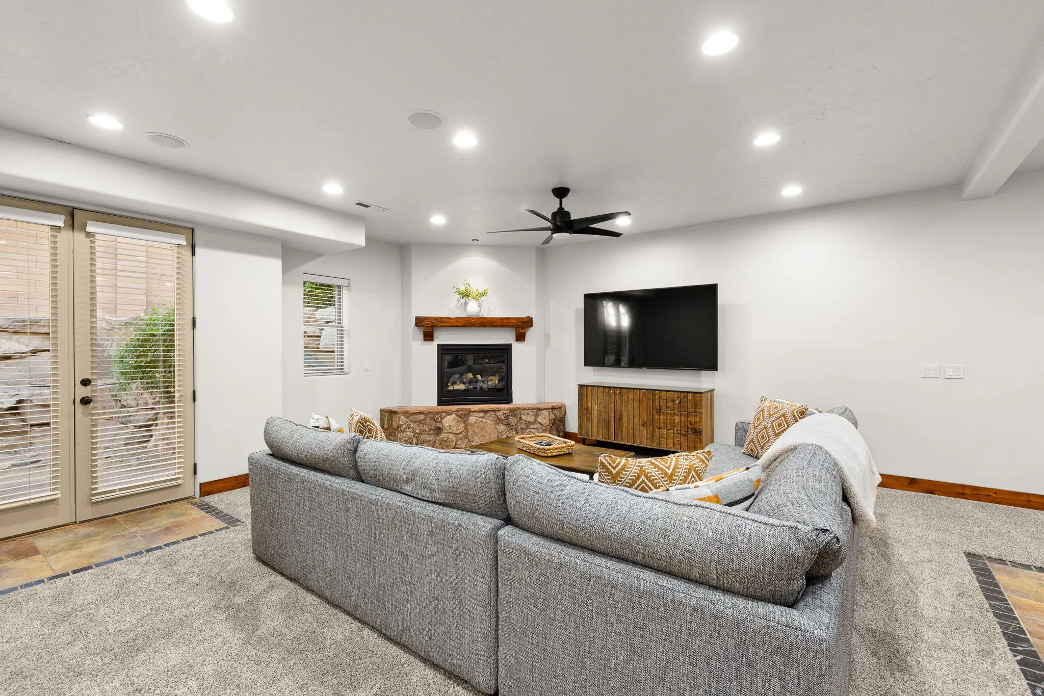 Living room featuring a ceiling fan, a glass covered fireplace, recessed lighting, light carpet, and french doors