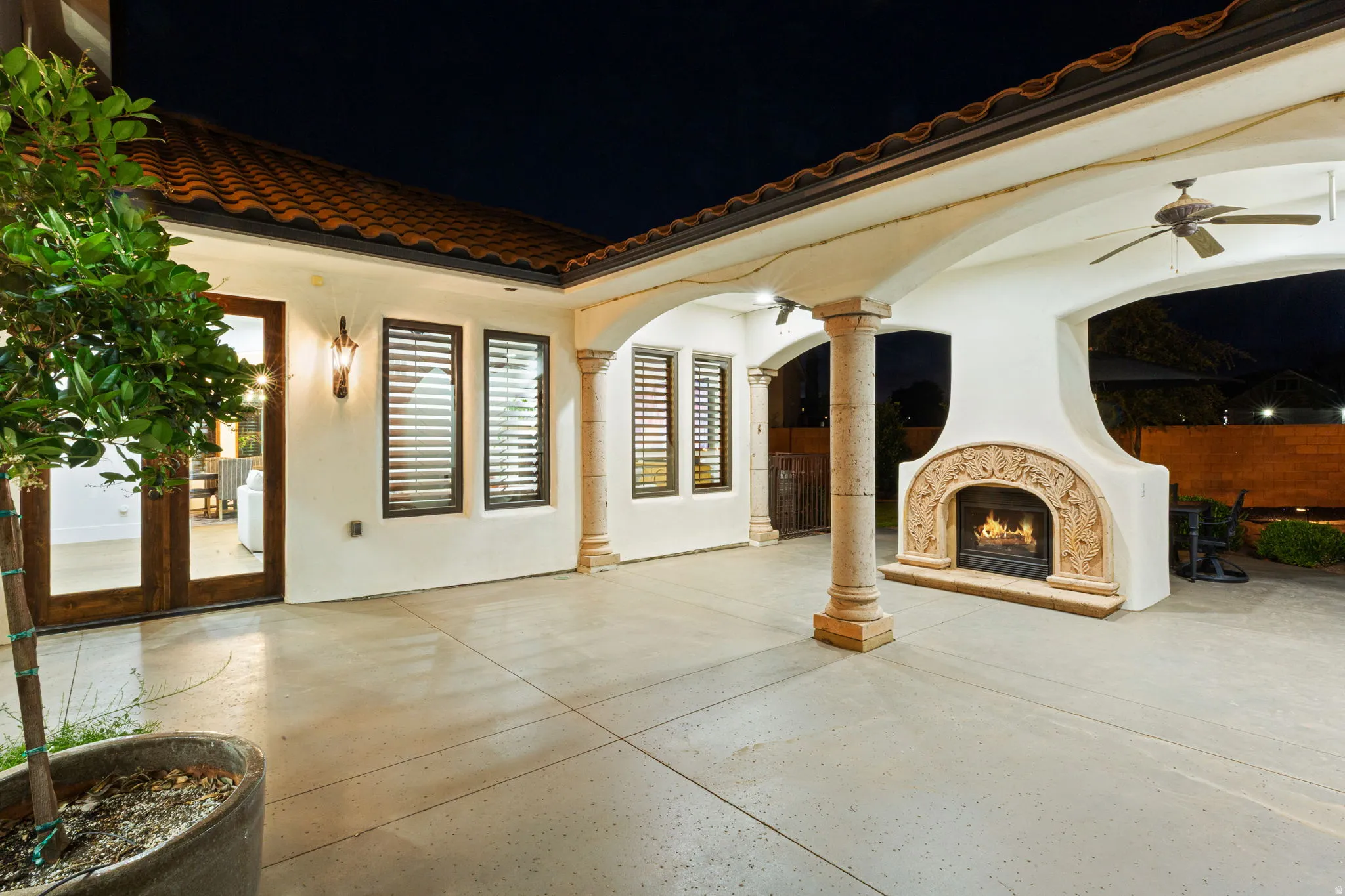 Covered outdoor patio featuring a decorative stone fireplace, tiled roofline, ceiling fans, and concrete flooring