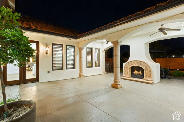 Covered outdoor patio featuring a decorative stone fireplace, tiled roofline, ceiling fans, and concrete flooring