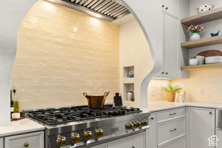 Kitchen featuring white cabinetry, stainless steel gas cooktop, open shelves, light stone countertops, and tasteful backsplash