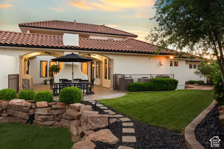 Back of house at dusk with a ceiling fan, outdoor dining area, a patio area, stucco siding, and a lawn