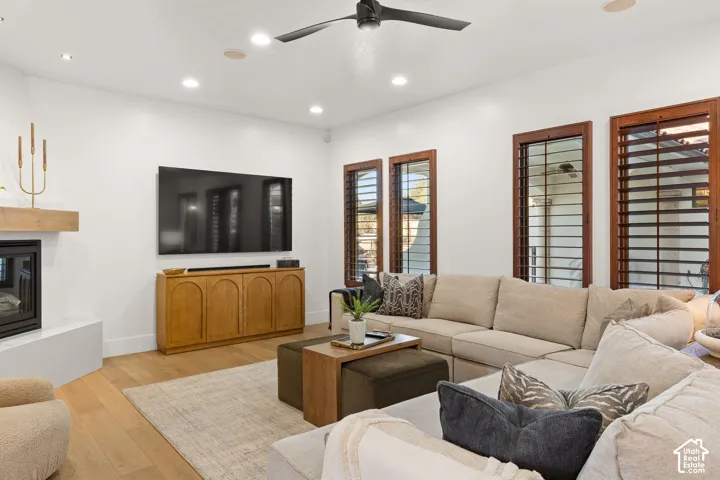 Living area with recessed lighting, light wood-type flooring, a glass covered fireplace, and ceiling fan