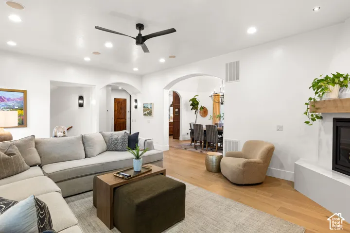 Living area with a glass covered fireplace, a ceiling fan, arched walkways, recessed lighting, and light wood-style floors
