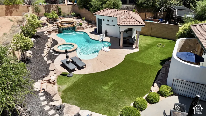 Backyard oasis featuring a freeform swimming pool with a waterfall, an integrated spa, a dedicated pool house with an attached covered patio, and a section of artificial turf