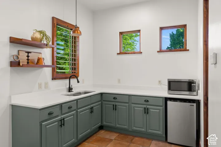 Kitchen featuring refrigerator, stainless steel microwave, decorative light fixtures, green cabinetry, and tile patterned floors