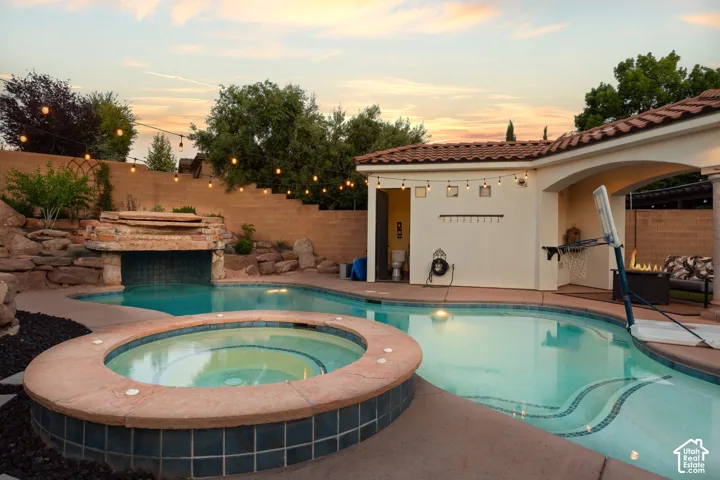 Pool at dusk featuring a fenced backyard, a patio area, and a pool with connected hot tub