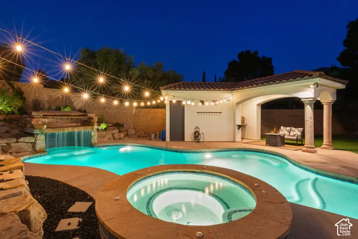 Resort-style backyard featuring a freeform swimming pool, integrated spa, rock waterfall feature, and covered patio with tiled roof
