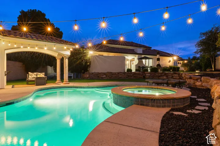 Resort-style backyard featuring a free-form swimming pool, integrated spa, and an arched covered patio with string lighting