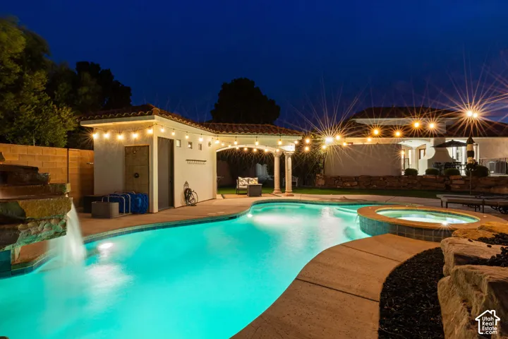 Custom-shaped swimming pool with an integrated spa, featuring a rock waterfall and perimeter lighting