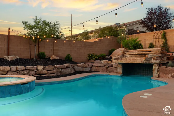 Pool at dusk with a fenced backyard and a pool with connected hot tub