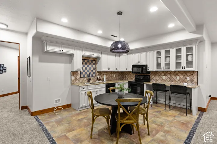 Kitchen featuring glass insert cabinets, white cabinetry, decorative backsplash, black appliances, and stone tile floors