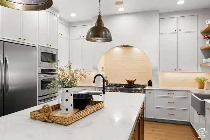 Dual tone kitchen featuring dual tone cabinetry, stainless steel appliances, light wood finished floors, light stone counters, and open shelves