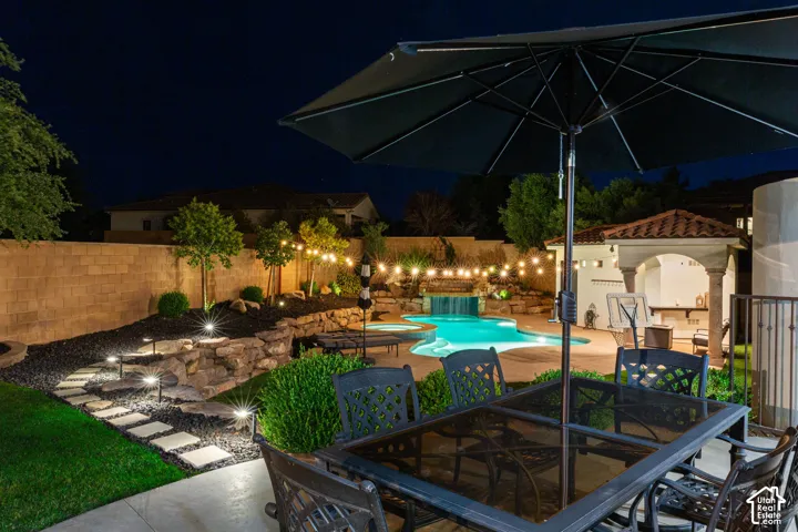 Resort-style backyard featuring a freeform swimming pool with a waterfall, an outdoor kitchen under a tiled pergola, and string lighting