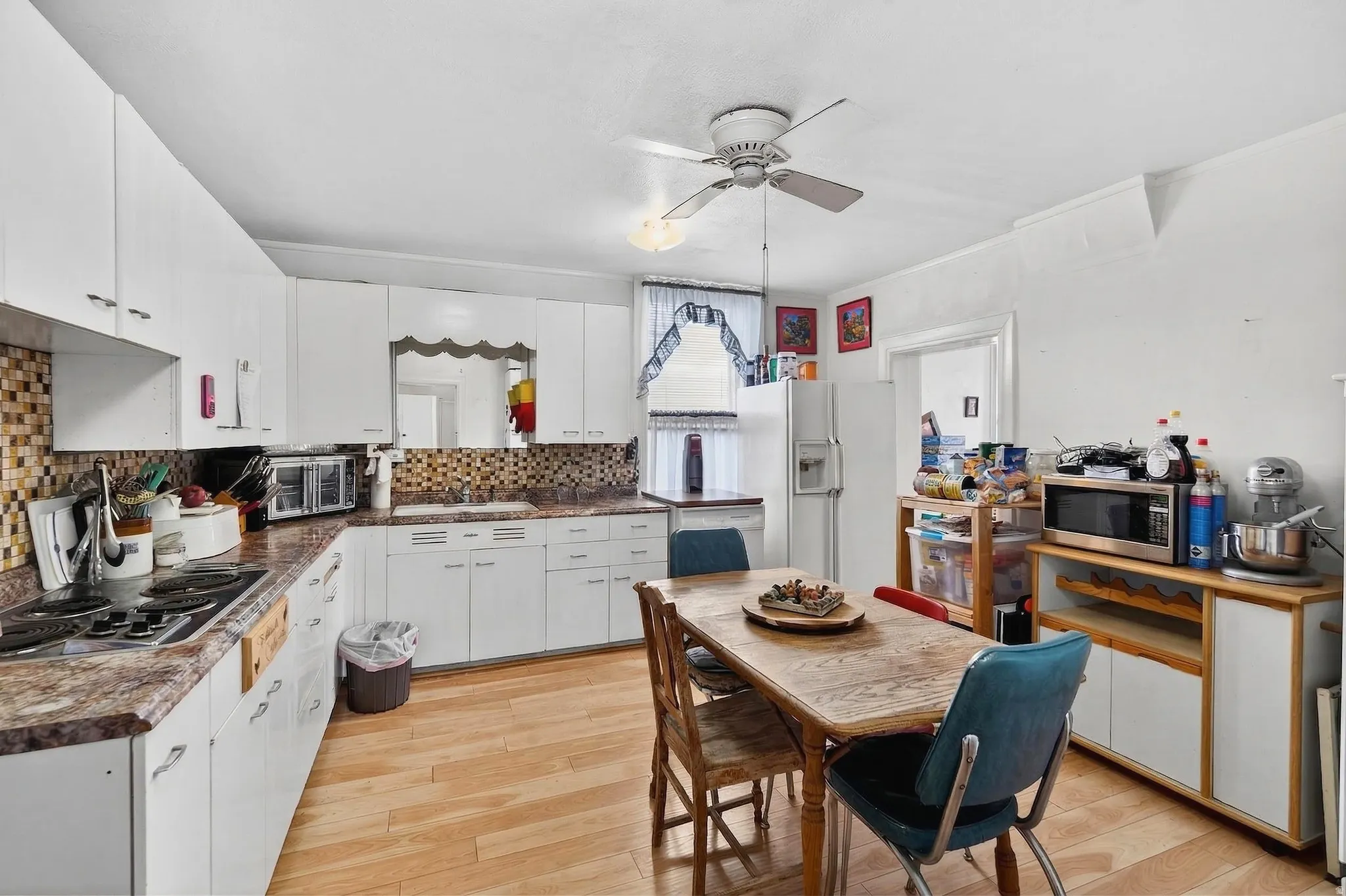 Kitchen featuring stainless steel appliances, light wood-style flooring, white cabinets, a ceiling fan, and ornamental molding