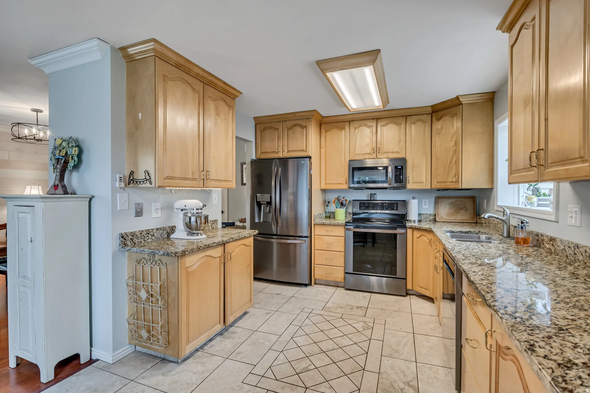 Kitchen featuring light stone countertops, stainless steel appliances, suspended lighting, and light wood finish cabinetry