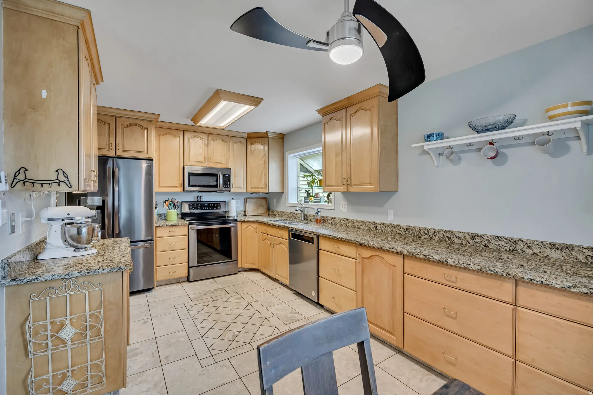 Kitchen featuring light wood finish cabinetry, light stone countertops, a ceiling fan, and stainless steel appliances