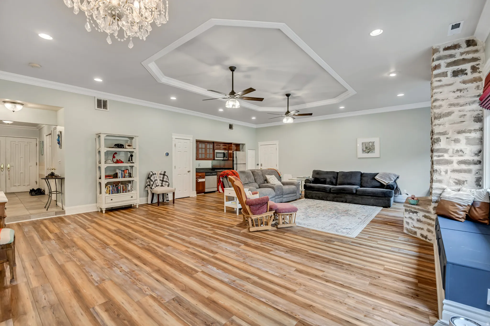 Living room with a tray ceiling, light wood finished floors, a chandelier, crown molding, and a ceiling fan