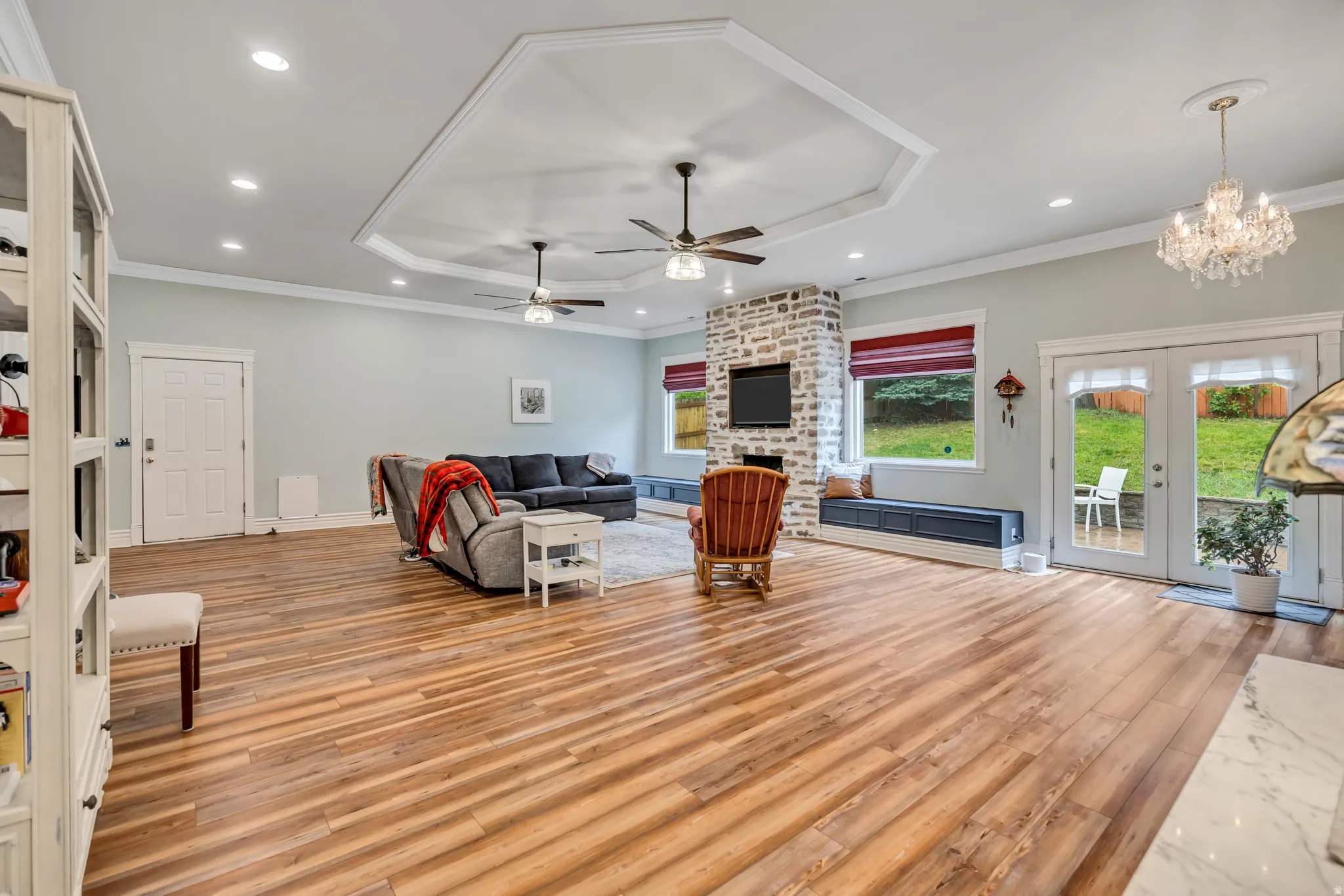Living room featuring french doors, a tray ceiling, light wood-style floors, hanging lights, and a fireplace