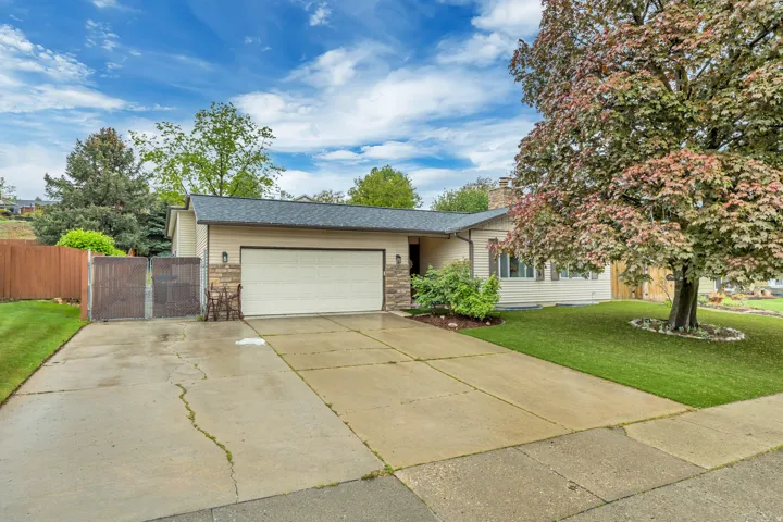 View of front of house with a gate, concrete driveway, an attached garage, stone siding, and a chimney
