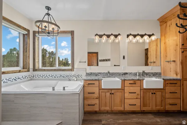 Bathroom with double vanity, a chandelier, a bath, and dark wood finished floors