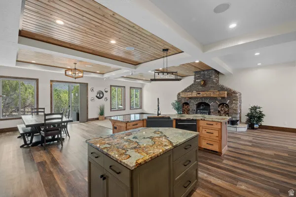 Two tone kitchen featuring open floor plan, a fireplace, light stone counters, dark wood-type flooring, and hanging lights