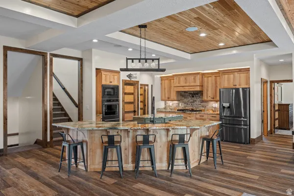 Kitchen with light stone countertops, wood ceiling, stainless steel refrigerator with ice dispenser, dark wood-type flooring, and a breakfast bar area
