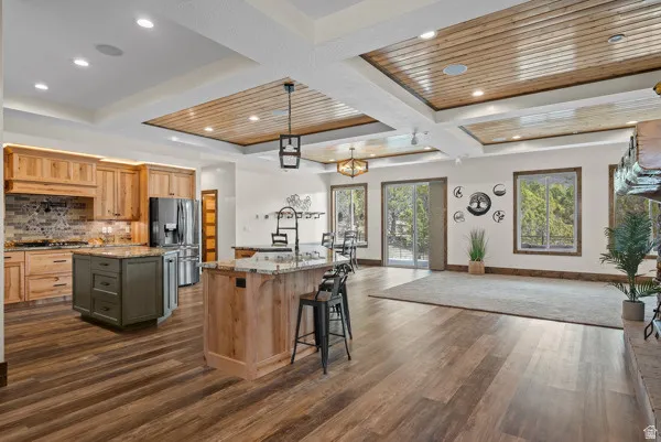 Kitchen featuring light stone counters, coffered ceiling, open floor plan, dual tone cabinetry, and stainless steel fridge