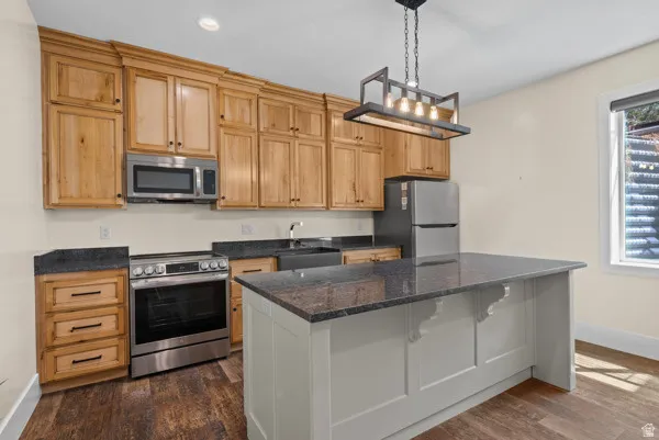 Kitchen with stainless steel appliances, a center island, dark stone counters, dark wood finished floors, and pendant lighting