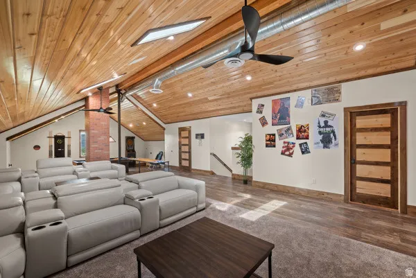 Cinema with ceiling fan, dark carpet, and a wooden ceiling with exposed beams