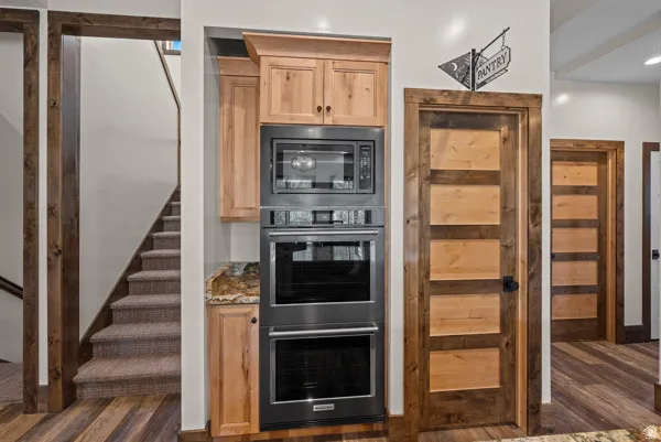 Kitchen featuring stainless steel double oven, stone counters, built in microwave, light wood finish cabinets, and dark wood finished floors