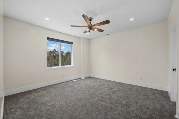 Unfurnished room with dark carpet and a ceiling fan