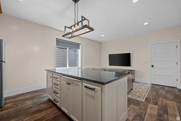 Kitchen with open floor plan, pendant lighting, dark stone countertops, a kitchen island, and dark wood-type flooring
