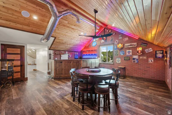 Dining space featuring brick wall, dark wood-style floors, a ceiling fan, and beamed ceiling