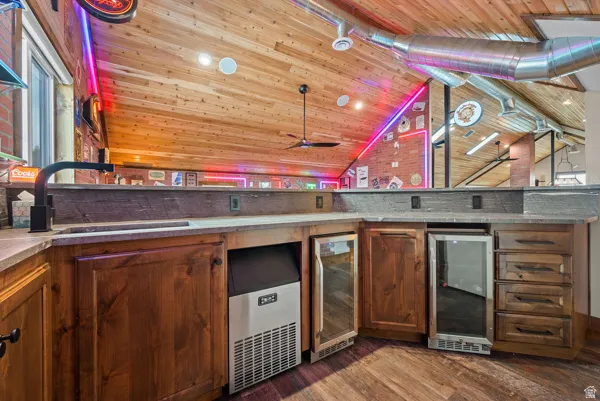 Indoor bar featuring dark wood-type flooring, wine cooler, wooden ceiling, and wood finish cabinets