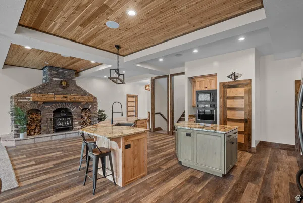 Dual tone kitchen featuring wood ceiling, a fireplace, light stone countertops, dark wood-type flooring, and wall oven