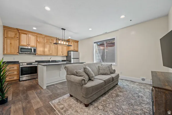Kitchen featuring stainless steel appliances, dark countertops, dark wood-style flooring, hanging light fixtures, and a kitchen island
