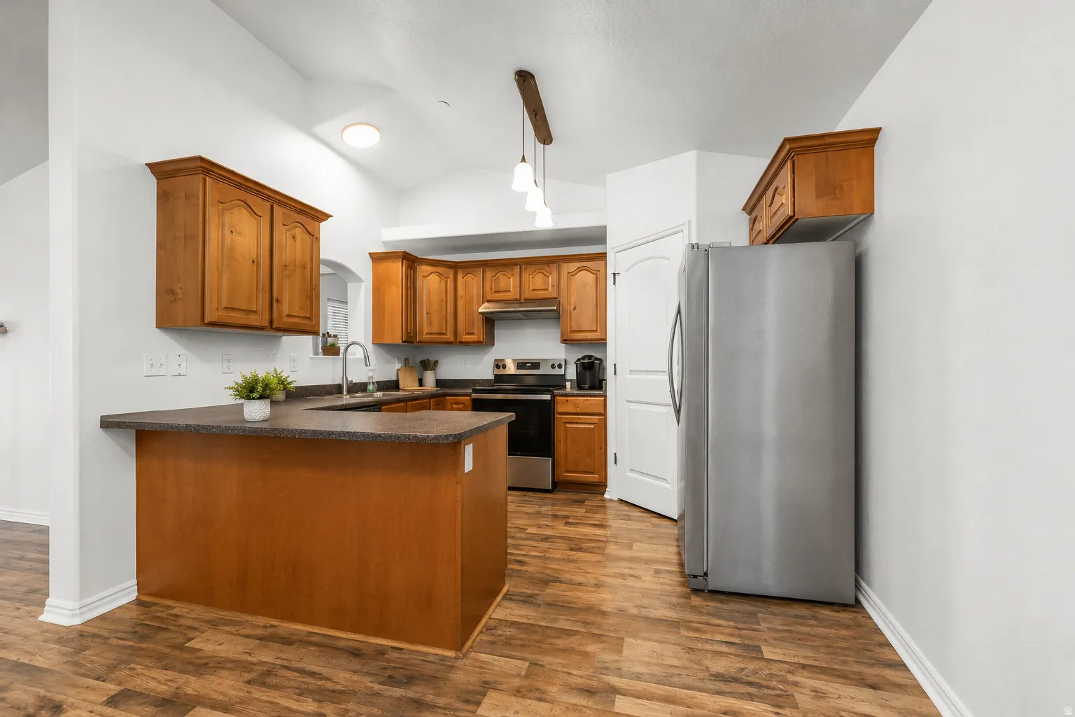 Kitchen featuring wood-finish flooring, warm wood cabinetry, a built-in kitchen island, stainless steel appliances, and a vaulted ceiling
