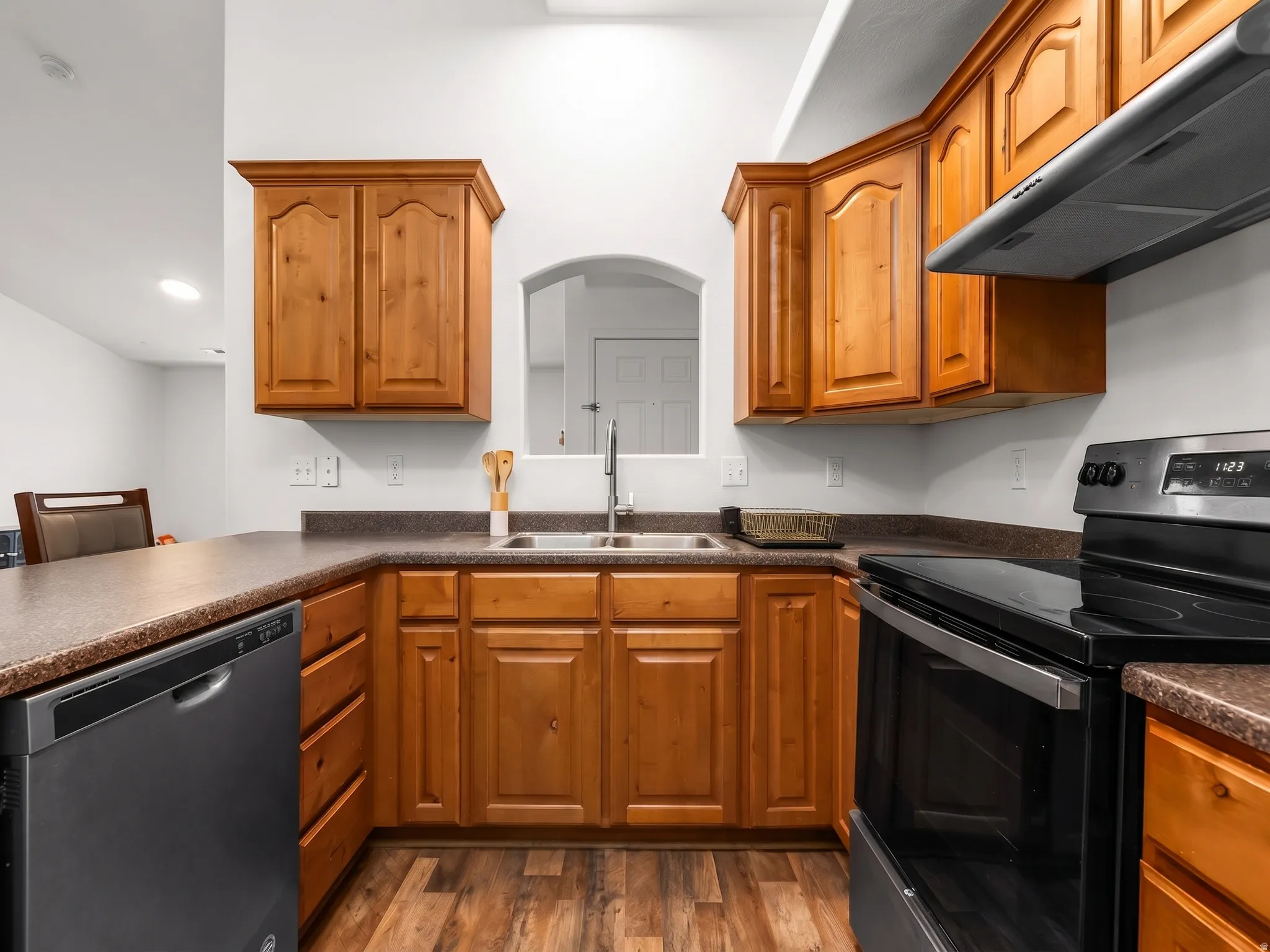 Kitchen with stainless steel appliances, dark countertops, ventilation hood, and wood finish cabinetry