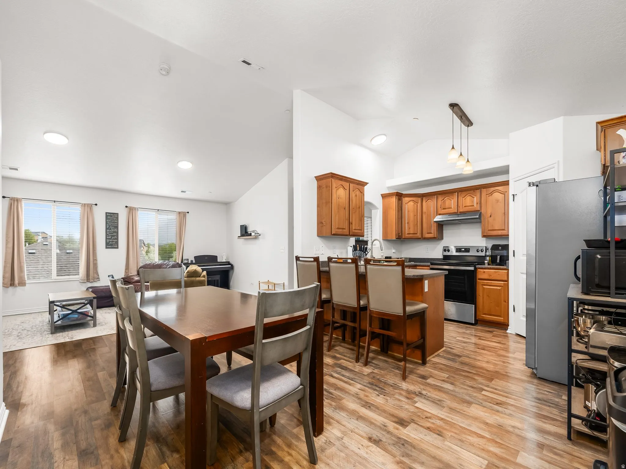 Vaulted ceilings, wood-finish flooring, kitchen island with seating, pendant lighting, and ample cabinetry