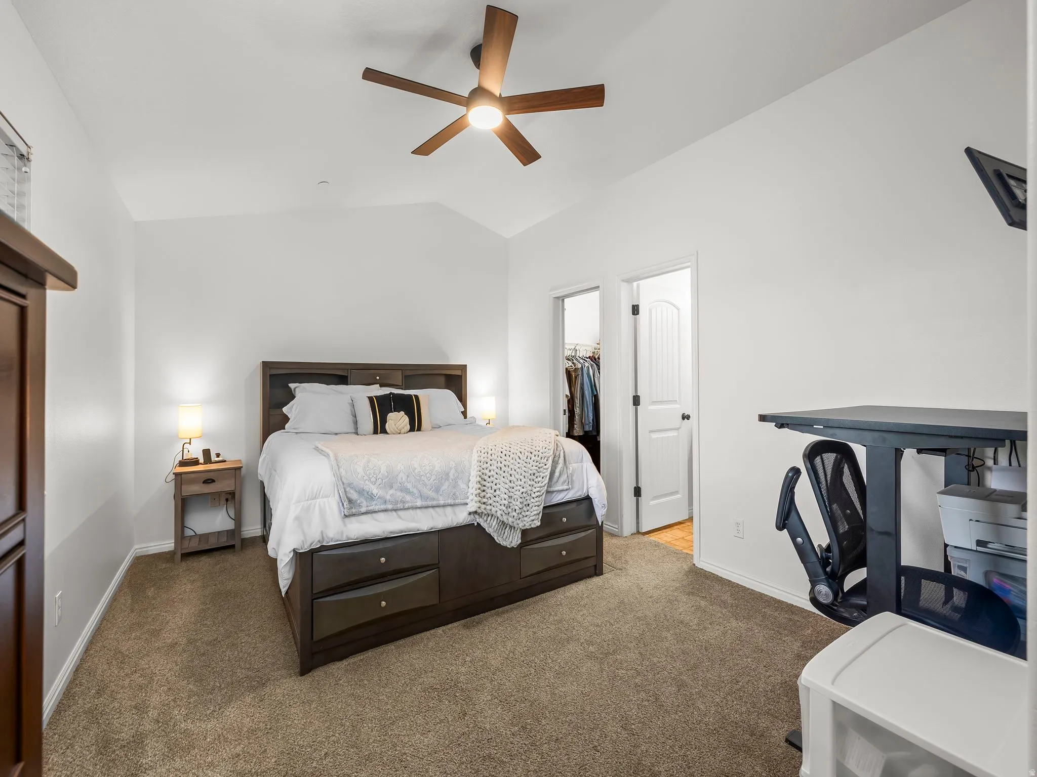 Vaulted ceiling with a wood-finish ceiling fan, carpeted flooring, and white interior doors