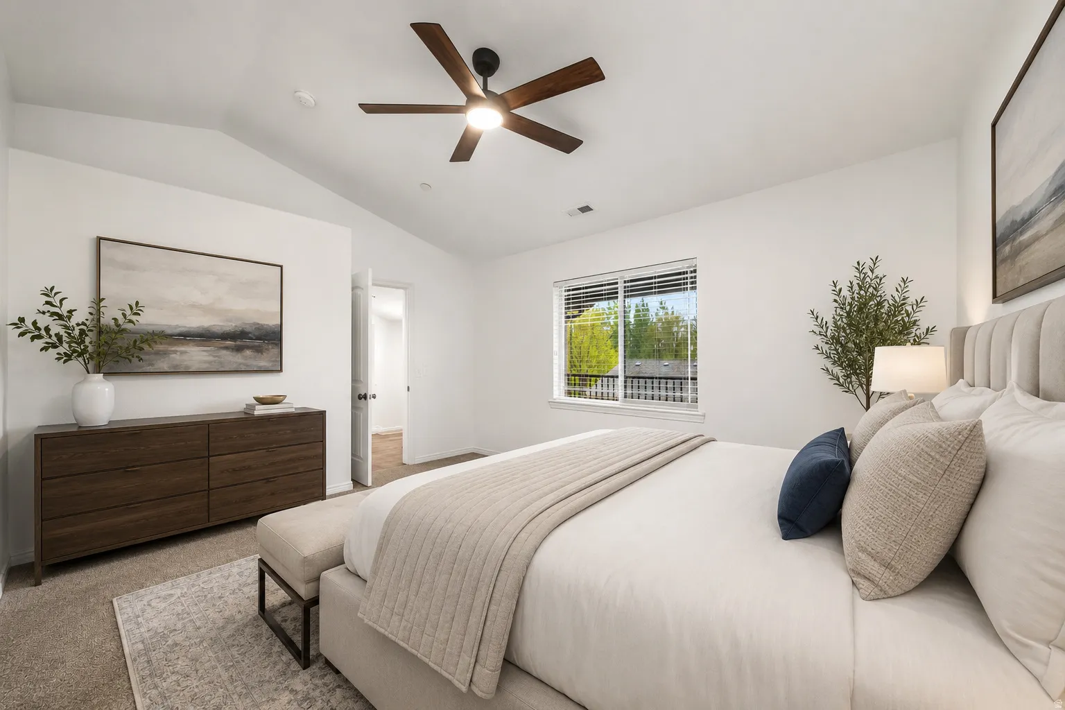 Serene primary bedroom featuring a upholstered headboard with nailhead detailing, wood-finish dresser, ceiling fan with integrated lighting, large windows with outdoor vistas, and neutral bedding in soft tones